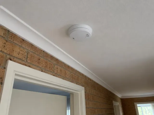 White smoke alarm mounted on a textured ceiling above a brick hallway in Manly Vale